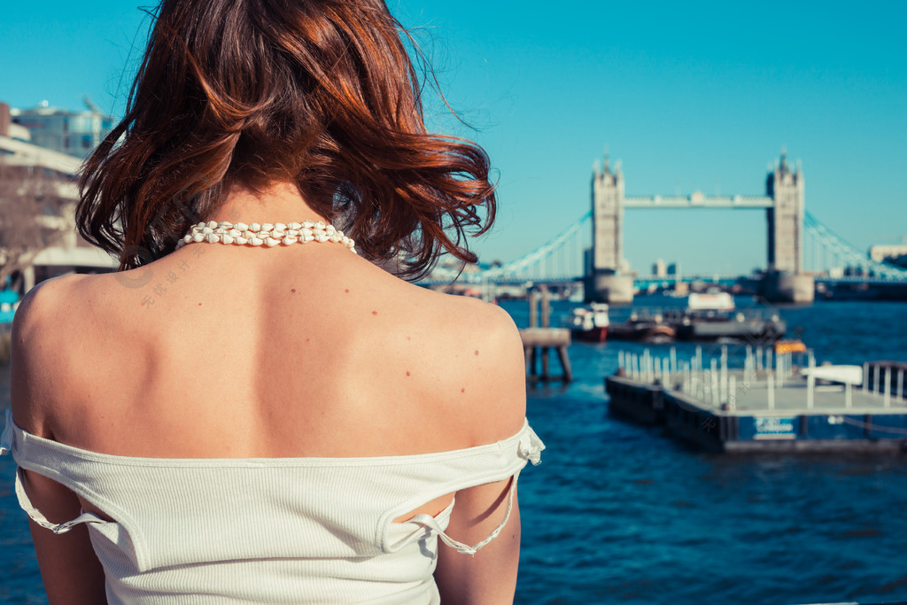 一个年轻的女人在阳光明媚的日子晒黑她的背看着英国伦敦的泰晤士河