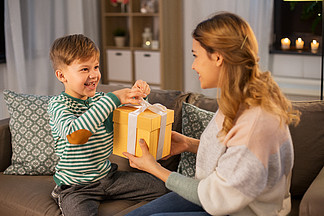 母亲节，假日和家<i>庭</i>观念-微笑的母亲给礼物她愉快的小儿子在家在晚上母亲送礼物给她的小儿子在家里