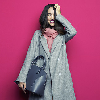 时尚的年轻时尚的女人，在紫红色的背景工作室照片灰色外套，粉色围巾，紫色唇膏，皮包目录衣服和配件<i><i>看</i></i><i><i>看</i></i>书