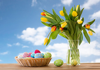 <i>复</i>活节，假日，传统和对象概念-在篮子和郁金香的色的鸡蛋开花在蓝天背景篮子和鲜花的<i>复</i>活节彩蛋