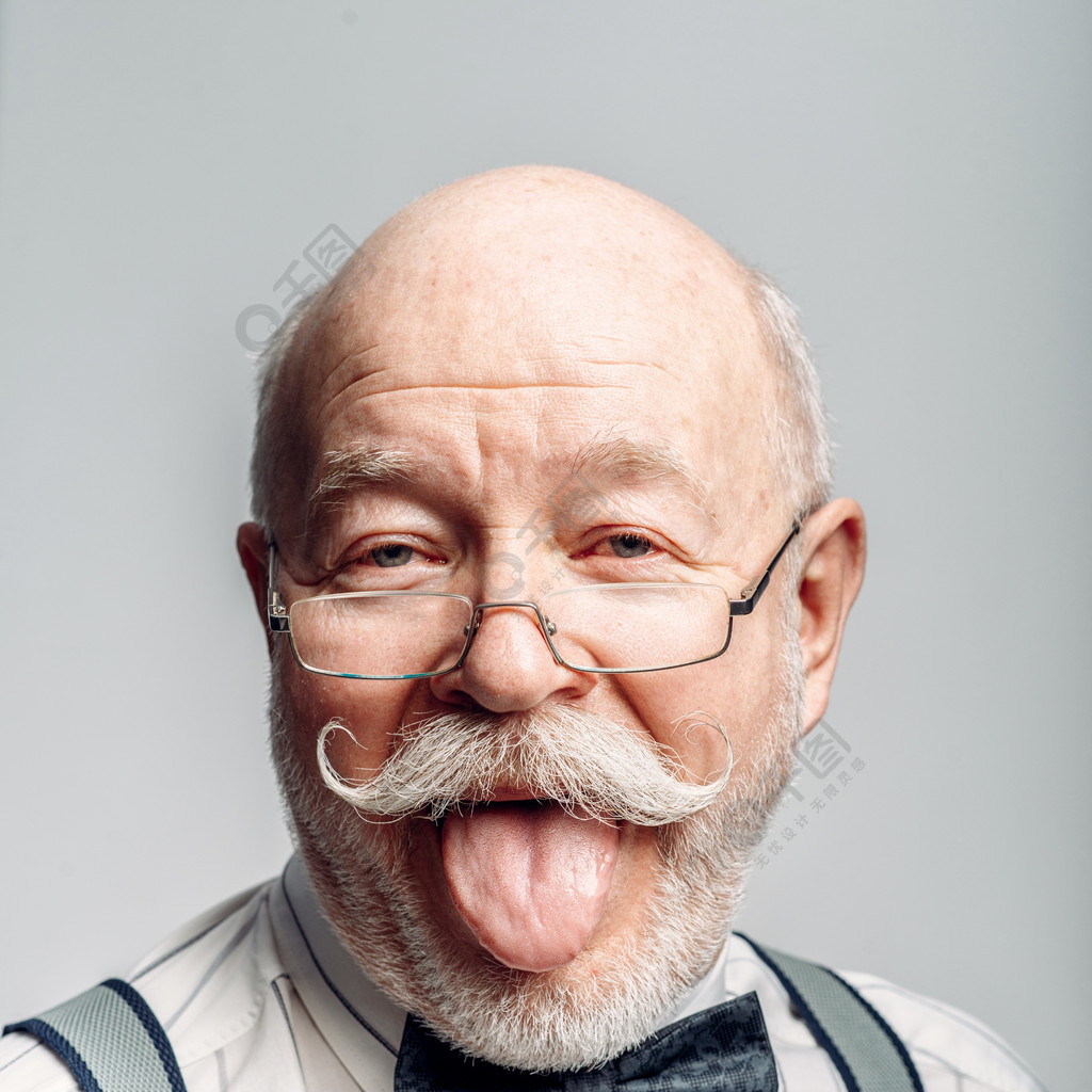 蝶形领结的和玻璃成熟资深看的照相机在演播室老人显示他的舌头的肖像