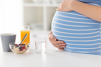 怀孕，健康饮食和产科概念-接近孕妇在家接触她的有早餐的腹部在厨房用桌上孕妇摸她的肚子的特写