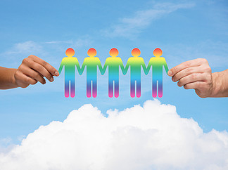 社区，团结和团队合作的概念-多种族夫妇手里拿着纸链同性恋者剪影在蓝蓝的天空，白<i>色</i>的<i>云</i>背景