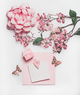俏丽的粉红彩笔贺卡嘲笑与开花装饰，心脏，一点礼物盒和弓在白色书桌背景，顶视图，平的位置婚礼请柬<i>布</i>局或母亲节的概念