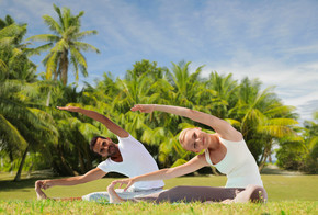 健身，体育和人们的观念-夫妇在异国情调的自然背景与棕榈树在户外做瑜伽练习幸福的夫妻，在户外做瑜伽练习