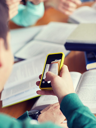 人，教育，技术和考试的概念— —用智能手机拍照的书页和在学校图书馆制作<i>备</i><i>忘</i>单的学生手的特写