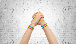 <i>lgbt</i>，同性关系和同性恋概念-接近戴着同性恋自豪感了悟腕带的男性手做在砖墙背景的赢取的姿态与同性恋骄傲腕带在胜利手势的手