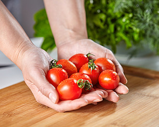 有机樱桃番茄被保存在一个女孩的手，呈现与新鲜蔬菜白色厨房的桌子上的一块木板文本的空间女孩的手拿着在一个木板的成熟西红柿在桌上用荷<i>兰</i><i>芹</i>复制文本空间
