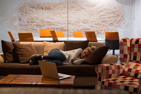 睡觉在沙发上的一个年轻偶然女商人在一个工休期间在一个创造性的办公