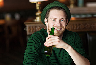 人，休闲和圣帕特里克节的概念— —快乐的年轻人，戴着帽子从瓶在酒吧或酒馆喝啤酒的快乐年轻男子的画像从绿色的瓶子，在酒吧或酒馆喝啤酒的人