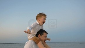 慢动作斯坦尼康来拍摄镜头的父亲和儿子在海滩上的飞机起飞中玩男孩坐在爸爸的肩膀上