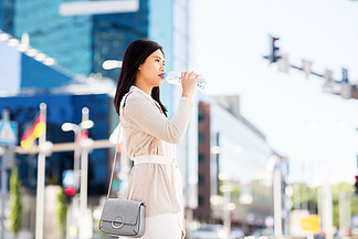 生活方式和人们观念-年轻亚裔妇女饮用水flom塑料瓶在城市从瓶在城市中的亚裔女子喝水