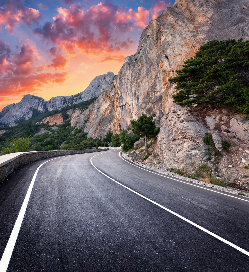 柏油路与美丽的弯曲的山路的五颜六色的风景有与高岩石,在日落的惊人