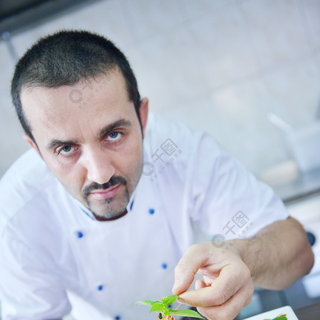 英俊的厨师穿着白色的制服在现代厨房装饰面食沙拉和海鲜鱼