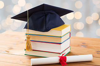 教育，学校，毕业和知识的概念— —在假期灯背景木制的桌子上关闭书和学位帽与文凭