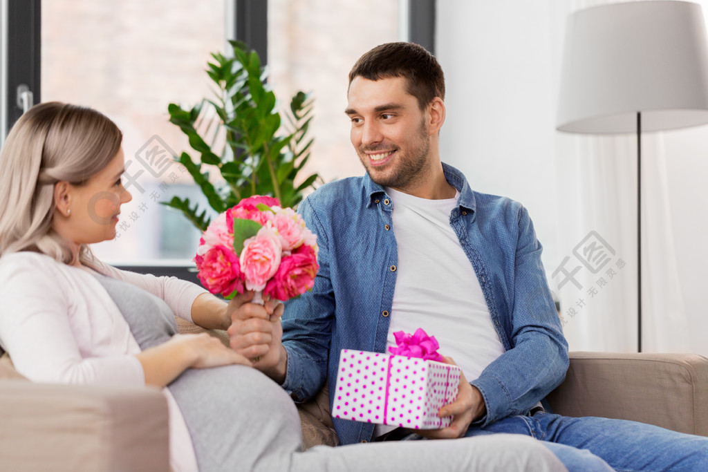 假日,懷孕和問候概念-在家給花的愉快的人孕婦男人給孕婦在家送花