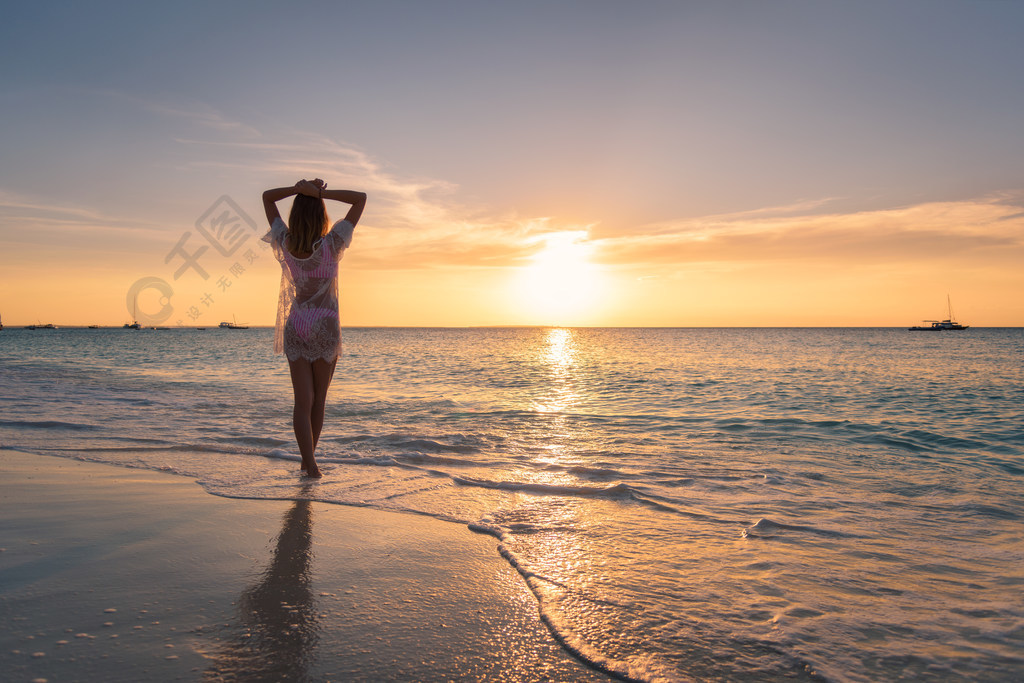 美丽的年轻女子在日落沙滩站在大海波浪对橙色的天空夏季旅行快乐苗条