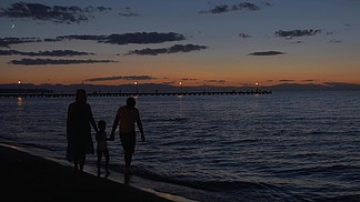 母亲，父亲和儿子手牵着手，在黄昏时赤脚走在海边黑色剪影与黑暗的大海，天空和背景中的码头