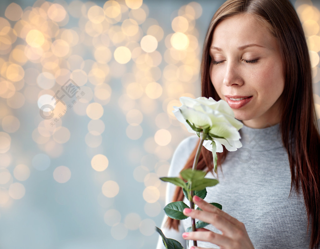 人和花的概念幸福的年輕女人嗅到大白玫瑰在節日燈的背景女人在節日燈