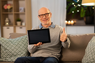 技术，晚年和人概念-有坐沙发和在家显示赞许的片剂个人计算机计算机的愉快的微笑的秃头老人在晚上平板电<i>脑</i>在家里快乐的老人