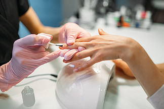 修指甲大师在粉红色的手套，将指甲涂在女性客户，美容院美甲师做指甲护理美容程序