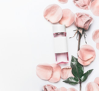 有面部玫瑰色水的化妆瓶或与精油，花和瓣的调色剂在白色书桌背景，顶视图，烙记的嘲笑和复制空间美容和皮肤护理概念