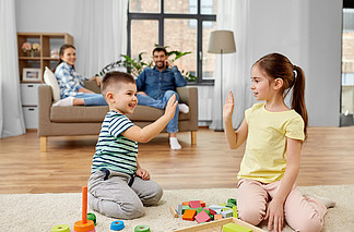 童年，休闲和家<i>庭</i>观念-哥哥和妹妹在玩木制玩具积木和做高五的手势哥哥和妹妹在家里玩玩具积木