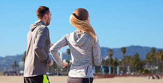 健身，体育，人们和健康的生活方式的概念— —幸福的夫妇，跑在威尼斯海滩背景在加利福尼亚州幸福的夫妇，在户外跑步幸福的夫<i>妻</i>在户外跑步
