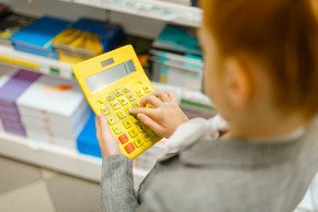 小女小学生拿着黄色计算器，购物在文具店女孩买的办公用品在商店，小学生在超级市场女学生持有计算器，文具店