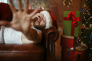 坏圣诞老人以说谎在沙发，讨厌的党，幽默的宿酒不健康的生活方式，有胡子的人，穿着节日服装，新年和酗酒坏圣诞老人与宿醉躺在沙发上