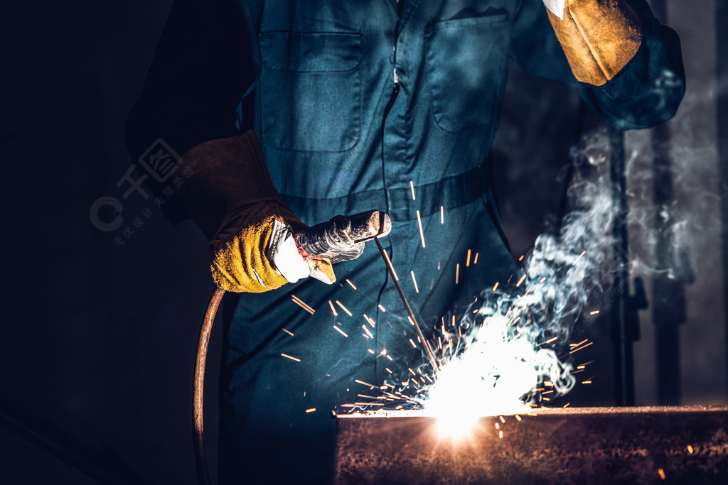金属焊工与弧焊机一起工作，在工厂焊接钢同时佩戴安全设备通过手工技能劳动概念的金属制品制造??和建筑维护服务