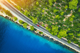 在夕阳春天美丽的绿色森林和海岸公路的鸟瞰图多彩景观道路上的车，蓝色的水，夏季树木从高速公路寄生虫的顶视图在克罗地亚旅行