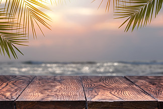 木桌上面在被弄脏的<i>海</i>的日落的有椰子树背景空准备好您的产品显示蒙太奇<i>海</i>滩的概念在夏天倒空木桌和棕榈叶在被弄脏的<i>海</i>滩背景