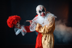 疯狂的血腥小丑在恐怖的红色假发中握住人类的头颅狂欢节服装，疯狂的疯子化妆的男人