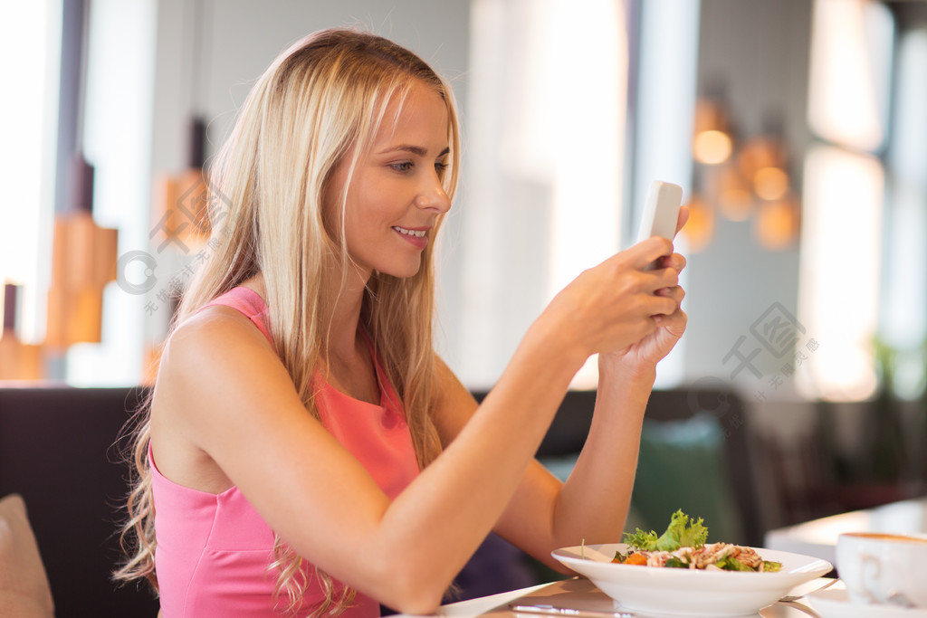 智能手机和沙拉在餐厅吃午饭的幸福女人智能手机在餐厅吃饭的校福