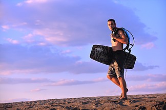 一个坚强的年轻冲浪人在日落时分在沉<i>思</i>的心情与冲浪板上海滩的肖像