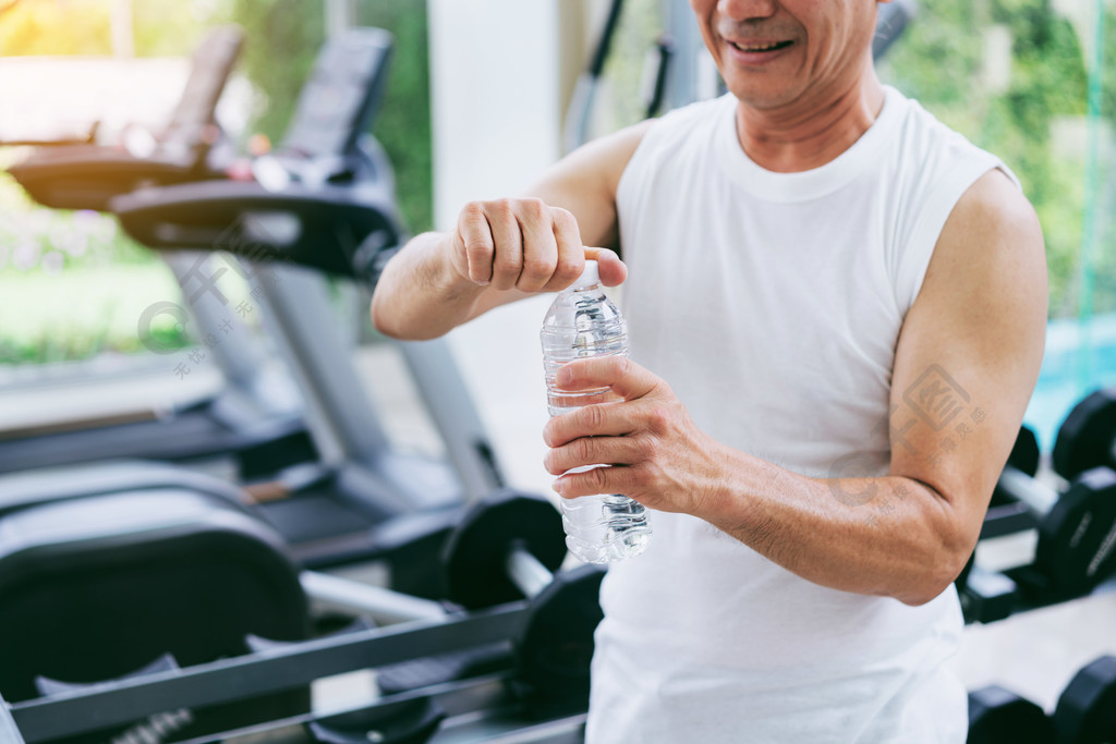 老人在运动后在健身房健身中心喝矿泉水老年人健康的生活方式