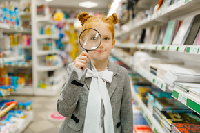 选择放大镜的小女小学生，购物在文具商店女童在商店里买办公用品，超市里的小学生