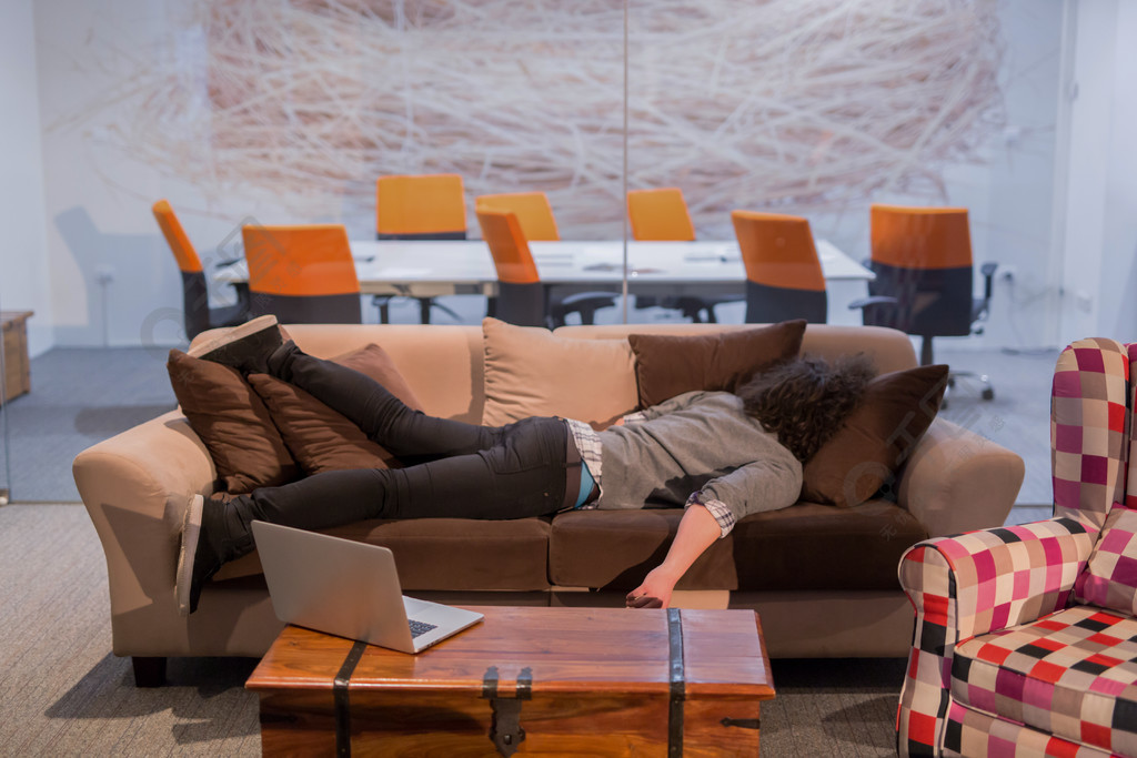 睡觉在沙发的一个年轻偶然商人在工休期间在一个创造性的办公室