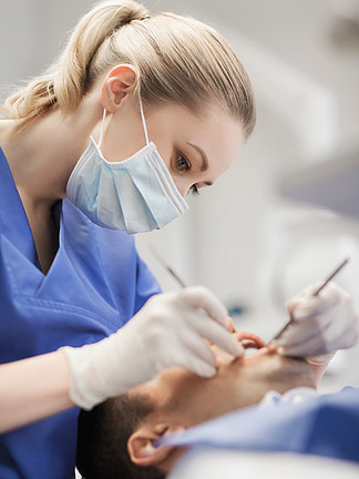 人，医学，口腔医学和卫生保健的概念— —女牙医用牙科镜和探针在牙科诊所办<i>公</i>室检查男性病人的牙齿