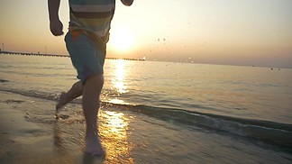 慢动作替身拍摄的赤脚在海岸上的水中奔跑的小孩美丽的景色与日落和无尽的大海，在背景中