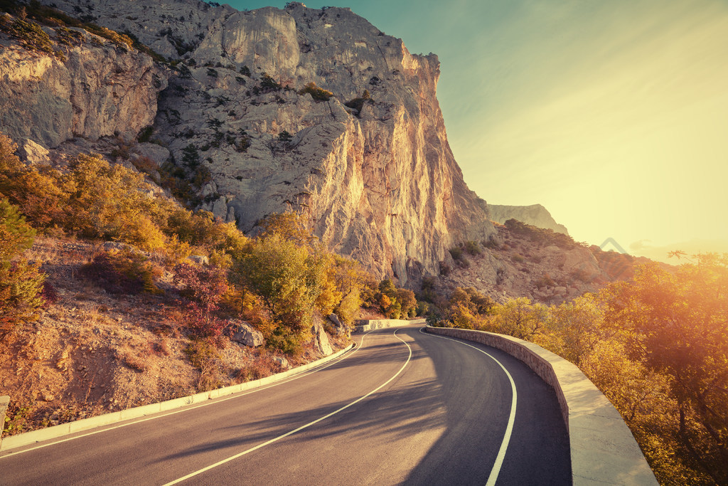 柏油路与美丽的山路与完美的沥青的多彩景观高岩石在日出的蓝天在夏天