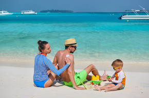 在海滩的家庭，年轻加上三岁的男孩应用防晒霜在人的后面的妇女保护化妆水 s在马尔代夫的暑假