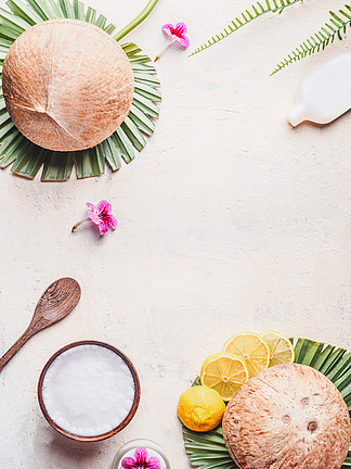 在木碗的椰子油有匙子和润湿的奶油的在白色书桌背景与热带叶子和花，顶视图帧复制空间平躺现代皮肤护理和化妆品的概念