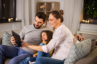 家<i>庭</i>，人们和技术概念-愉快的微笑的父亲，母亲和小女儿有片剂个人计算机计算机的在家在晚上平板电脑在家里幸福的家<i>庭</i>，在晚上