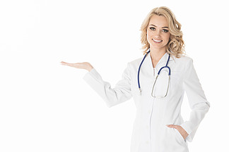 白色外套的微笑的女性<i>医</i><i>生</i>指向用手棕榈的空的拷贝空间，在白色背景隔绝的演播室白大褂的<i>医</i><i>生</i>用一只手指向