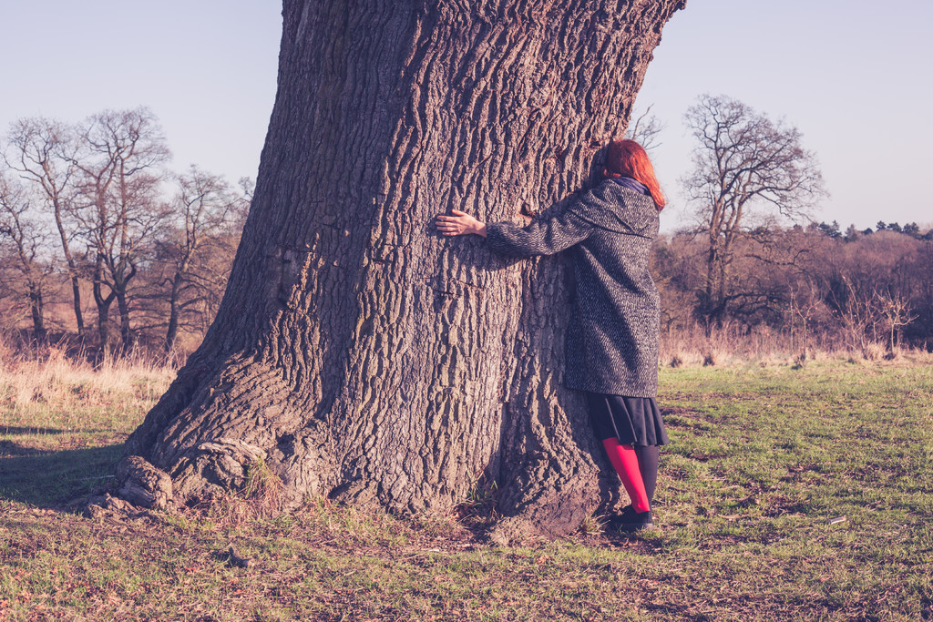 一个年轻女子在寒冷的冬天里抱着一棵大树