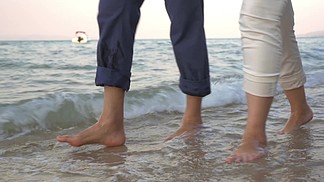 斯坦尼康来拍摄镜头的两人的赤脚在传入的海浪中漫步在海边