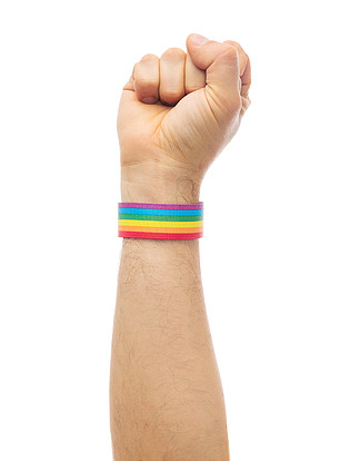 <i>lgbt</i>，同性关系和同性恋概念-接近显示拳头的男性手佩带的同性恋自豪日知名度袖口与同性恋骄傲彩虹腕带的手显示拳头同性恋骄傲彩虹腕带的手显示拳头