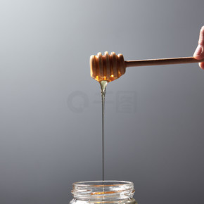 木棍子用自然花蜂蜜在一张灰色具体桌上的一只妇女手上，文本的地方上传统的有用的天然甜味女人的手握住一根木棒与灰色背景上滴水葵花蜜在一个玻璃瓶犹太新年健康假期